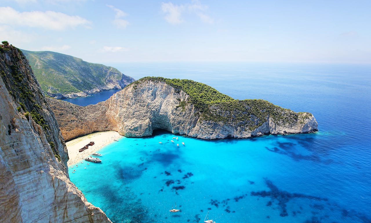 why-choose-us Stunning aerial view of Navagio Beach in Zakynthos, Greece, featuring turquoise water and a sunken ship.